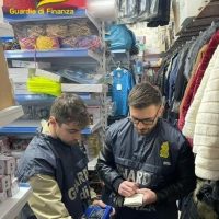 Due uomini in uniforme all'interno di un negozio, uno controlla qualcosa sulle mani dell'altro tra scaffali e abbigliamento esposto.