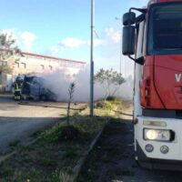 Autocarro dei vigili del fuoco in azione su strada, fumo visibile e personale all’opera vicino a edifici civili.