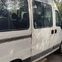 Furgone bianco con finestra laterale, parcheggiato in strada, parzialmente all’ombra di alberi.