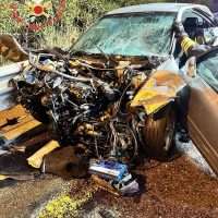 Auto schiacciata da un incidente stradale: blocchi incastrati, paraurti sfondato, soccorritori e parti sparpagliate sull’asfalto.