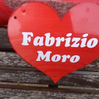 Cuore rosso con scritte bianche: Fabrizio Moro, su sfondo legno.