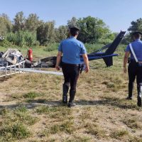 Due uomini sorridenti si avvicinano a un piccolo aereo sportivo in un campo erboso, sotto cielo sereno.