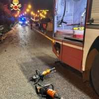 Scena notturna di incidente: autocarro fermo su stradina, pneumatici e attrezzi a terra, luci di fari e segnaletica, atmosfera di soccorso.