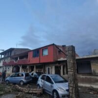 Edificio residenziale a due piani colorato, veicoli parcheggiati di fronte e cielo sereno con nuvole.