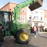 Gru manegevole escavatore verde con la benna sollevata, intorno gente in piazza davanti a edificio. Scene urbana e attivo in mostra.