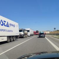 Automobile sullo svincolo autostradale con camionware in coda, strada a tre corsie e cielo sereno, veicoli in fila verso la distanza.
