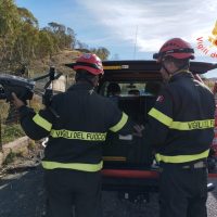 Due vigili del fuoco in divisa, con caschi rossi, vicino all'oblò di un'auto, su strada aperta e contesto di soccorso