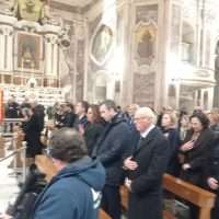 Interno di una chiesa affollata, pellegrini in pantofole o abiti sobri in fila tra colonne e dipinti sacri, partecipano a una funzione religiosa.