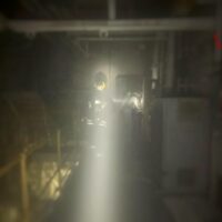 Visione interna di un ambiente industriale sfocato con una retromarcia di luce luminosa al centro, attrezzature e scaffalature sullo sfondo.