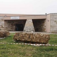 Edificio moderno in stile architettonico con ingressi a forma di pyramide e pareti in pietra; giardino con cespugli e tappeto erboso davanti all’ingresso.