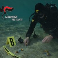 Subacqueo dei Carabinieri osserva oggetti segnalati in sabbia marina: attestazioni di indagine in campo visivo sotto acqua.