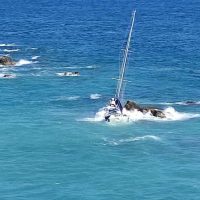 Vela al rallentatore tra acque turchesi e onde leggere, su scogli bianchi; panoramica marina di una giornata soleggiata.