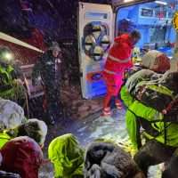 Soccorritori al lavoro in una scena di emergenza: equipe infermieristica e vigili del fuoco assistono feriti in condizioni di freddo, ombrelli e attrezzature.