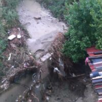Trasbordo di terra e detriti su un pendio, con alberi, fango e massi, vicino a una zona coperte da vegetazione e rifiuti
