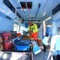 Ambulanza interna luminosa: soccorritore in abito giallo fluorescente controlla attrezzature mediche sistemate su sedili e cassette