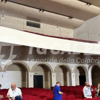Interior del Teatro all’aperto con palchi rossi e archi in stile arabo, persone al lavoro vicino ai sedili.