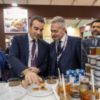 Due uomini in abito mostrano e assaggiano una selezione di conserve e marmellate su un banco in fiera gastronomica.
