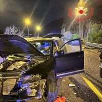 Auto da incidente su strada notturna, banchi e lampeggianti, cofani aperti e danni visibili, scena di soccorso vicino a una segnaletica.