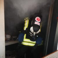 Soccorritore in tuta protettiva in mezzo al fumo, visiera e maschera, in un ambiente di incendio.