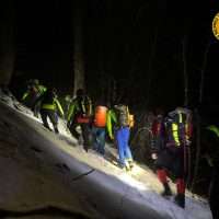 Escursionisti in salita notturna su pendio innevato, equipaggiamento al completo, luci retroilluminate, atmosfera di avventura e fatica.