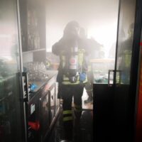 Scena di due vigili del fuoco in uniforme alzando una schermata fumo in un corridoio di negozio, luce intensa alle spalle.
