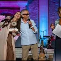 Gruppo di persone sul palco durante un evento, musica sullo sfondo, atmosfera luminosa e festosa in tonalità blu.