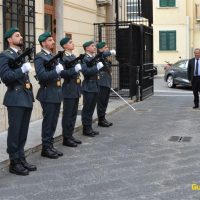 Soldati in uniforme allineati all'ingresso di un edificio storico, in attesa del passaggio di una persona in abito elegante.