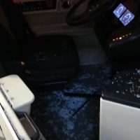 Interni di un autobus o veicolo: sedili scuri, pavimento blu scuro con riflessi, parte anteriore con cruscotto illuminato e display.