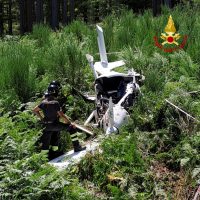 Scena di soccorso: elicottero atterra in una zona boschiva, soccorritori in tuta protezione vicino a macchina cha sorge tra erba alta.