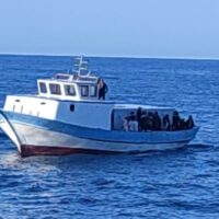 Barca da pesca o turismo sul mare azzurro, passeggeri a bordo con alberi di sole e onde calme.