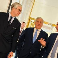 Gruppo di uomini in abiti formali che conversano in corridoio, tonalità professionale e atmosfera aziendale.