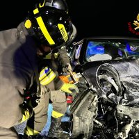 Intervento di soccorso automobilistico: vigili del fuoco sull’auto gravemente danneggiata, operano in sera luminosa, equipaggi in tuta.