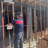 Poliziotto in divisa in sopralluogo in un cantiere, tra impalcature e gabine di legno, controllando l’area con una supervisione centrale.