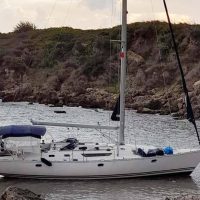 Barca a vela bianca ormeggiata vicino a una scogliera rocciosa, acque calme e cielo sereno.