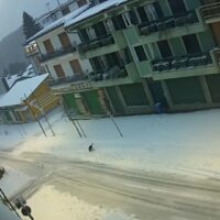 Strade innevate con edifici colorati a due piani, veicoli coperti di neve, atmosfera di pittoresco borgo montano