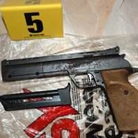 Collezione di reperti: pistola nera, carabina lunga, caricatore, rivestimenti e massiccia chiave rossa sullo sfondo; numero 5 giallo in alto a sinistra.