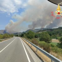 Straordinario panorama: strada retromarcia verso una collina fumante e fumo luminoso che avvolge il paesaggio, cielo azzurro.