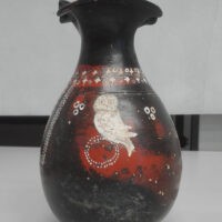 Vaso scuro a figura di oca bianca su sfondo rosso, decorazioni floreali; stile rustico, superficie leggermente usurata.
