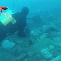 Subacquei tra reperti sommersi e mammiferi marini, esplorazione di un sito di immersione con attrezzatura e luce blu.