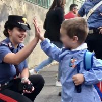 Due bambini in stato di gioia si salutano con un high five: una ragazza in uniforme di agente di polizia e un bambino sorridente con zaino, all’aperto.