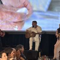 Concerto dal vivo con chitarrista al centro, pubblico sorridente in primo piano, scena ideale per un evento musicale in sala.