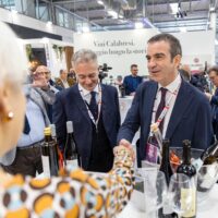 Professionisti al convegno brindisi in un salone affollato, bicchieri e bottiglie sul tavolo, discussioni tra relatori e partecipanti.
