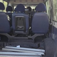 Interno di un pulmino con sedili blu, vista verso i posti posteriori e pezzi di metallo sul pavimento.