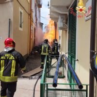 Vigili del fuoco in azione in una stradina stretta: fiamme e fumo emergono tra i palazzi, equipaggi al lavoro, Provvidenza e urgenza.