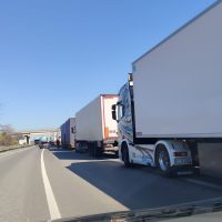 Autostrada con file di tir bianchi e camion industriali in fila, cielo azzurro limpido e corsia di emergenza sul lato destro.