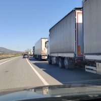 Auto in corsa sorpassa una fila di tir su un’autostrada, paesaggio desertico e cielo sereno.