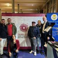 Gruppo di persone in fiera, stand con logo CALARIA e banner blu sullo sfondo, atmosfera informale e accogliente.