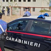 Automobile dei Carabinieri nera con strisce rosse, agenti in divisa blu monitorano una scena in un'area aperta.