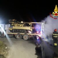 Addetti antincendio vicino a veicolo verricellato riflettori, fumo visibile, notte, operazione di soccorso e spegnimento.