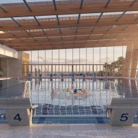 Piscina coperta all’aperto con tetto in legno, vasche e persone che si divertono sul bordo. Atmosfera serena, luce filtrata.